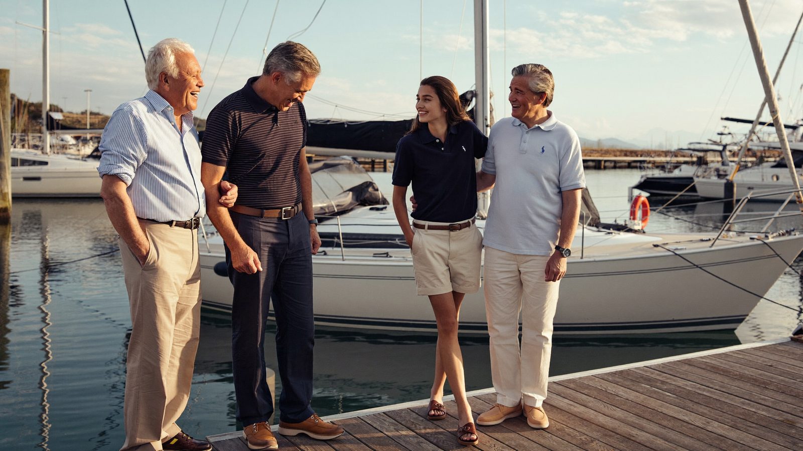 Four people of different ages, from their 20s to their late 60s, laughing together on a Long Island marina dock at golden hour