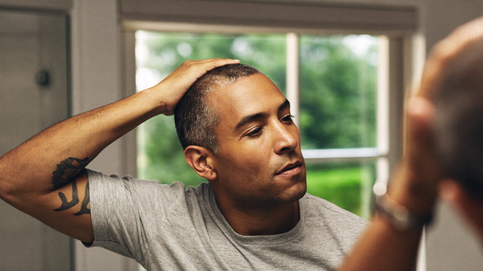 Man checking his healing hairline in a bathroom mirror about a week after a hair transplant