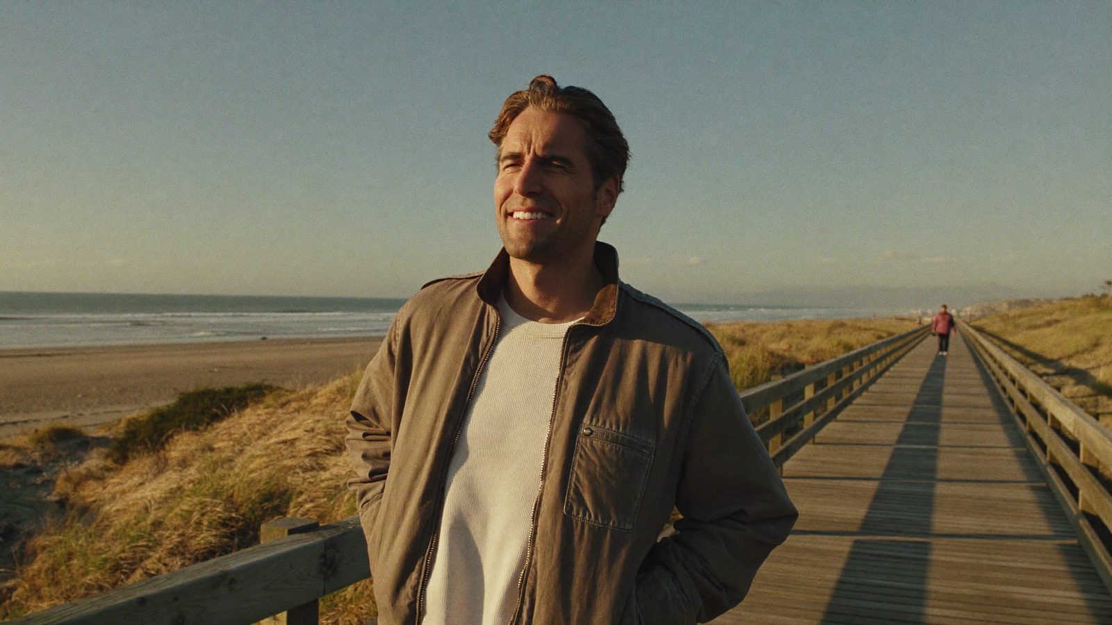Man in his late 30s walking on a beach boardwalk at golden hour