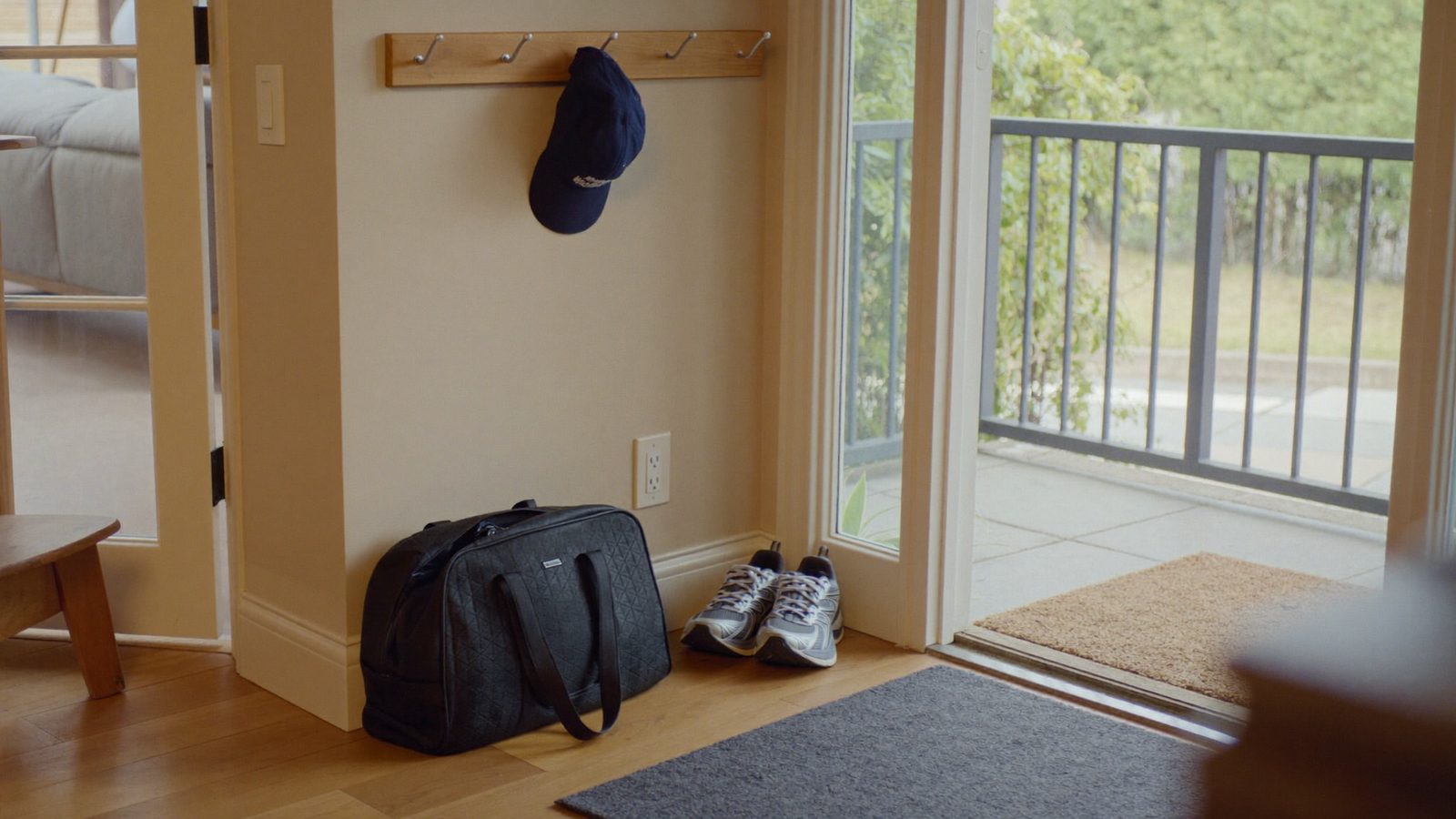Running shoes and a gym bag by a front door as a man hangs a baseball cap on a hook